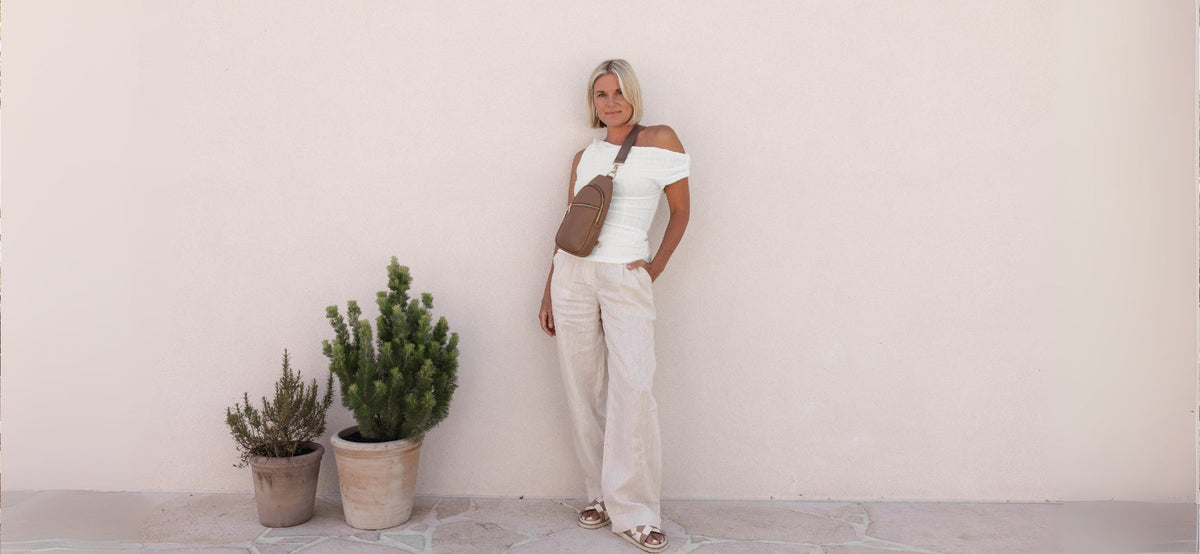 Woman stands in front of wall, wearing crossbody bag across her chest