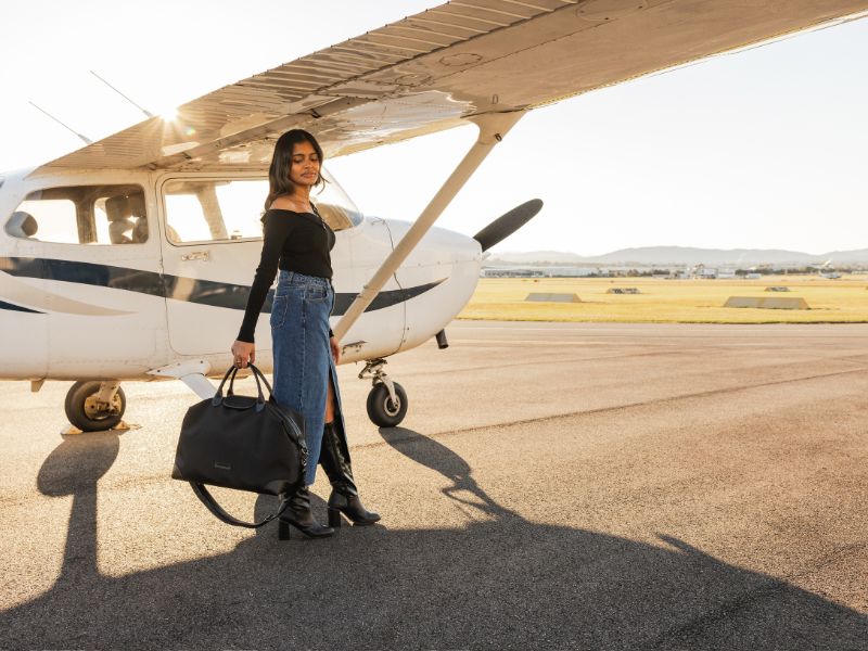 Woman holds black carry on bag while standing in front of aeroplane on tarmac