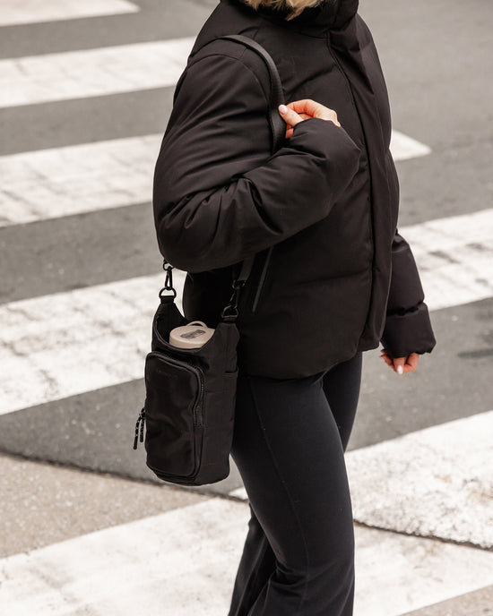 Louenhide Miami Water Bottle Bag in black nylon is worn over shoulder, styled with black leggings and jacket